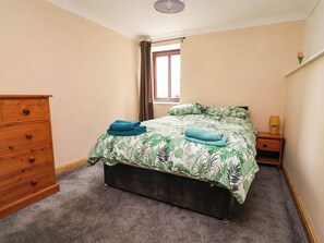 Une chambre à coucher avec un lit, une commode en bois, une table de chevet avec une lampe et une fenêtre avec des rideaux.