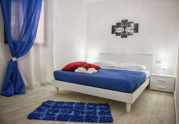 Ein Schlafzimmer mit einem Bett, einem Nachttisch, einem Wandbild und einem blauen Teppich.