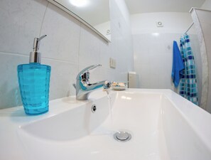 Ein Badezimmer mit einem weißen Waschbecken, einem chromfarbenen Wasserhahn und einer blauen Glas-Seifenspender.