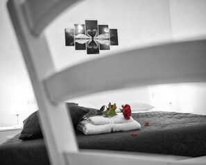 Ein Bett mit dunkler Decke, einem weißen Kopfkissen und einer roten Rose auf einem weißen Handtuch.