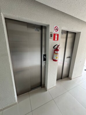 A hallway with two elevators, a fire extinguisher, and a no-smoking sign. - Cozy and fully equipped apartment, close to the shopping mall and tourist attractions! (Poços de Caldas)