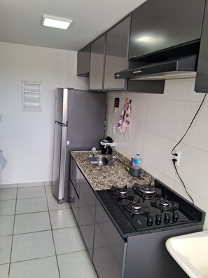 A kitchen with a stainless steel refrigerator, a gas stove, a sink, and a tiled backsplash. - Cozy and fully equipped apartment, close to the shopping center and tourist attractions! (Poços de Caldas)