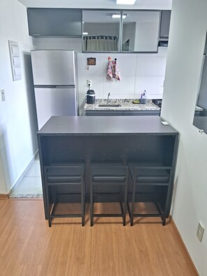 A compact kitchen with a built-in refrigerator, a sink, and a countertop. - Cozy and fully equipped apartment, close to the shopping mall and tourist attractions! (Poços de Caldas)