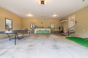 Une pièce comprenant une table de ping-pong, un petit coin bar, une horloge et un escalier.