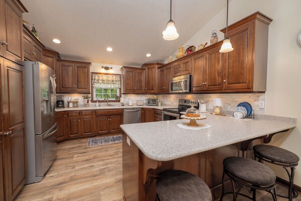 A kitchen with wooden cabinets, stainless steel appliances, a granite countertop, and bar stools.