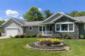 A two-story house with a stone facade, a front porch, and a well-maintained front yard with a flower bed and shrubs. - 4-BR home, custom kitchen, rec room, patio, grill. Near hiking & Amish country! (Dover)