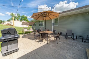 Une terrasse avec un barbecue, une table, des chaises et un parasol.