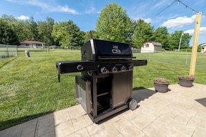 Un barbecue portable sur roulettes, portant les inscriptions « C3 » et « PRO SERIES », placé sur une surface pavée, avec une zone herbeuse et une clôture en arrière-plan.