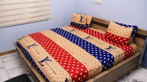 Cama com colcha estampada e almofadas combinando, cabeceira de madeira e piso de mármore.