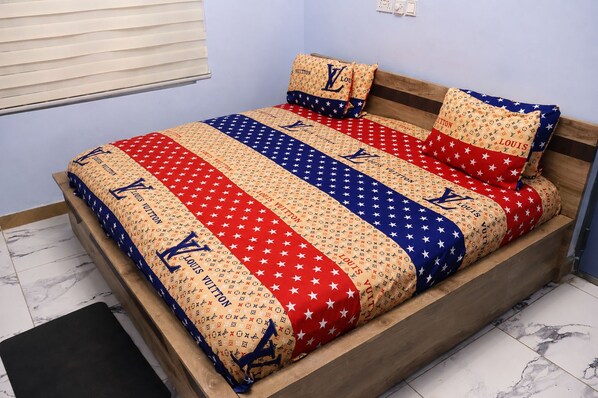 A bed with a patterned bedspread and matching pillows, a wooden headboard, and a marble floor.