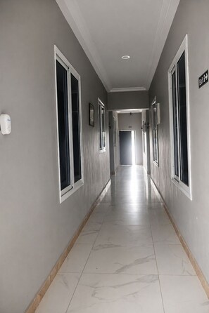 A corridor with doors on both sides, a hand sanitizer dispenser on the left wall, and a sign indicating an exit on the right wall.