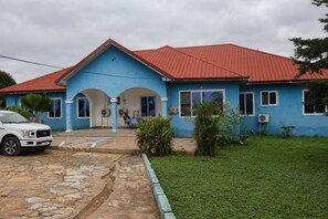 A blue house with a red roof, a driveway, and a parked white truck. - Pleasant 1-bedroom Queen with AC in vibrant Koforidua (Koforidua)