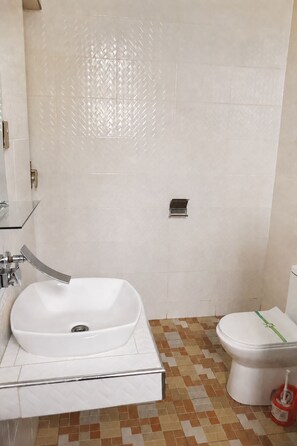 A bathroom with a white sink, a toilet, and a shower area. - Pleasant 1-bedroom Queen with AC in vibrant Koforidua (Koforidua)