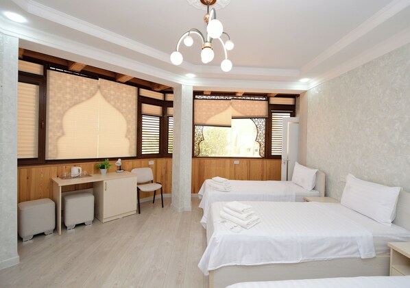A hotel room with two beds, a desk, a chair, and a window with blinds.