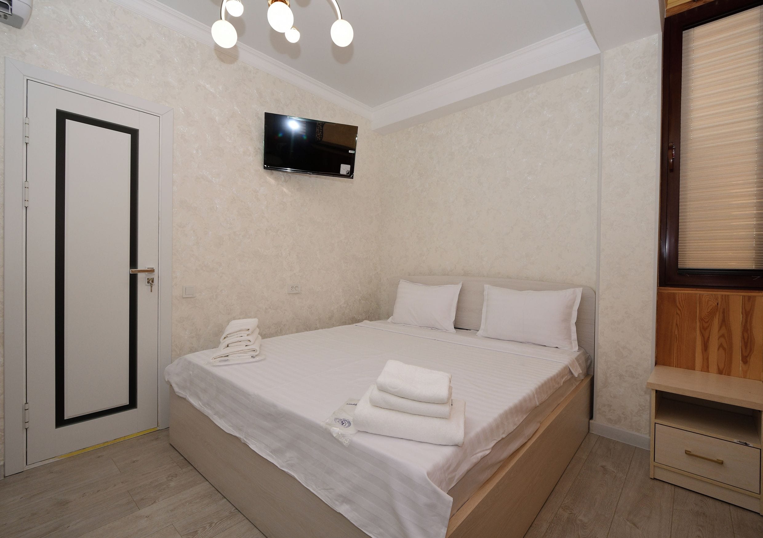 Une chambre à coucher avec un lit, un téléviseur fixé au mur, une porte et une armoire en bois.