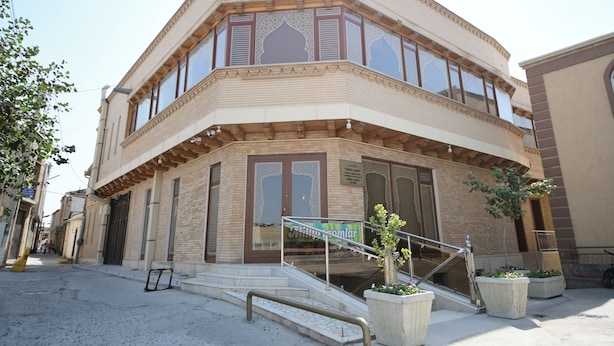Un edificio angolare a due piani, con un balcone e una scala che conduce all'ingresso.