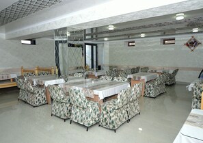 Un comedor con varias mesas y cabinas, piso de mármol y un techo alto con diseño geométrico.