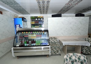 Pequeña habitación con un refrigerador de bebidas, un área de descanso con cojines estampados y una repisa con bebidas embotelladas.