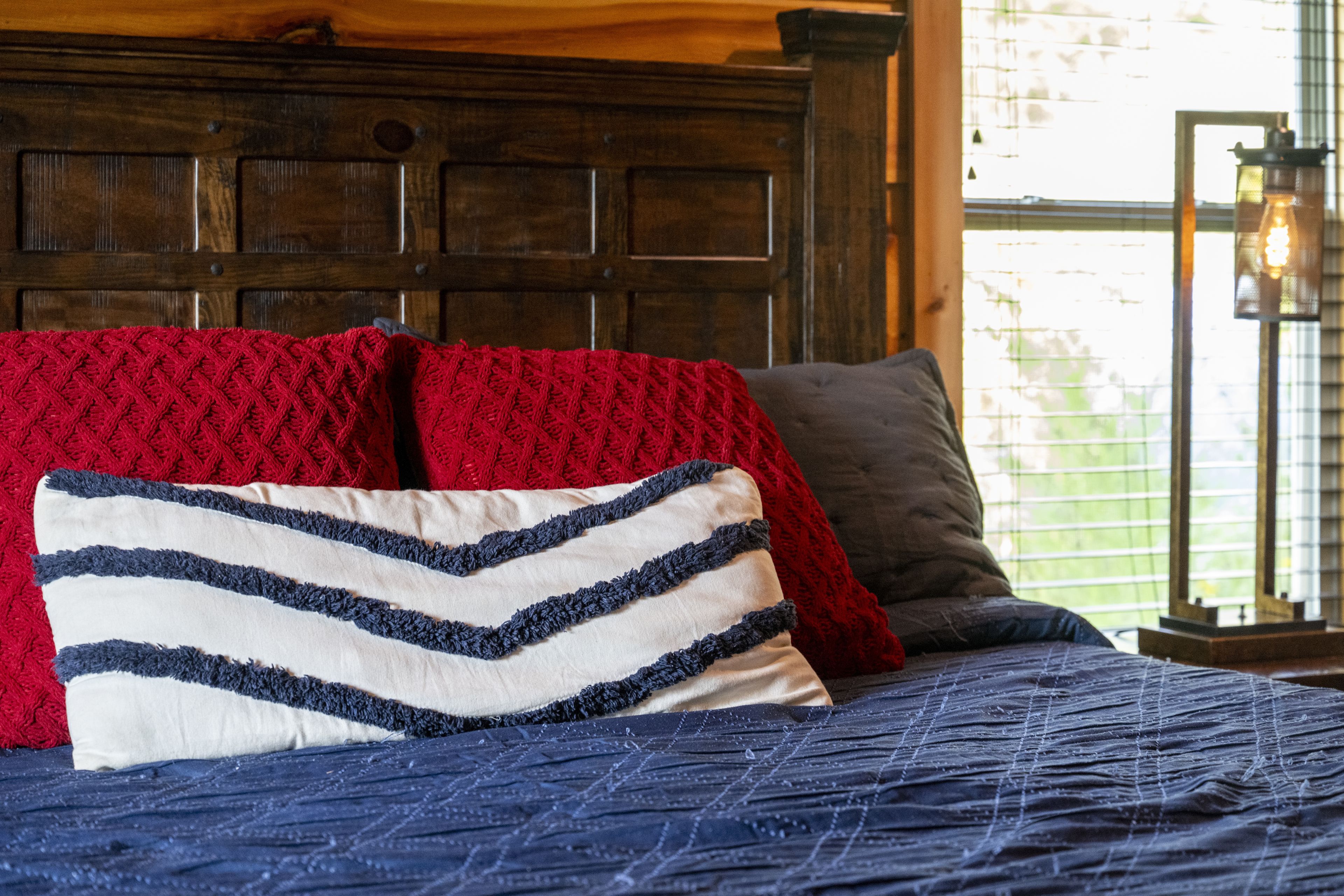 A bed with a dark blue quilt, red and white pillows, and a wooden headboard.