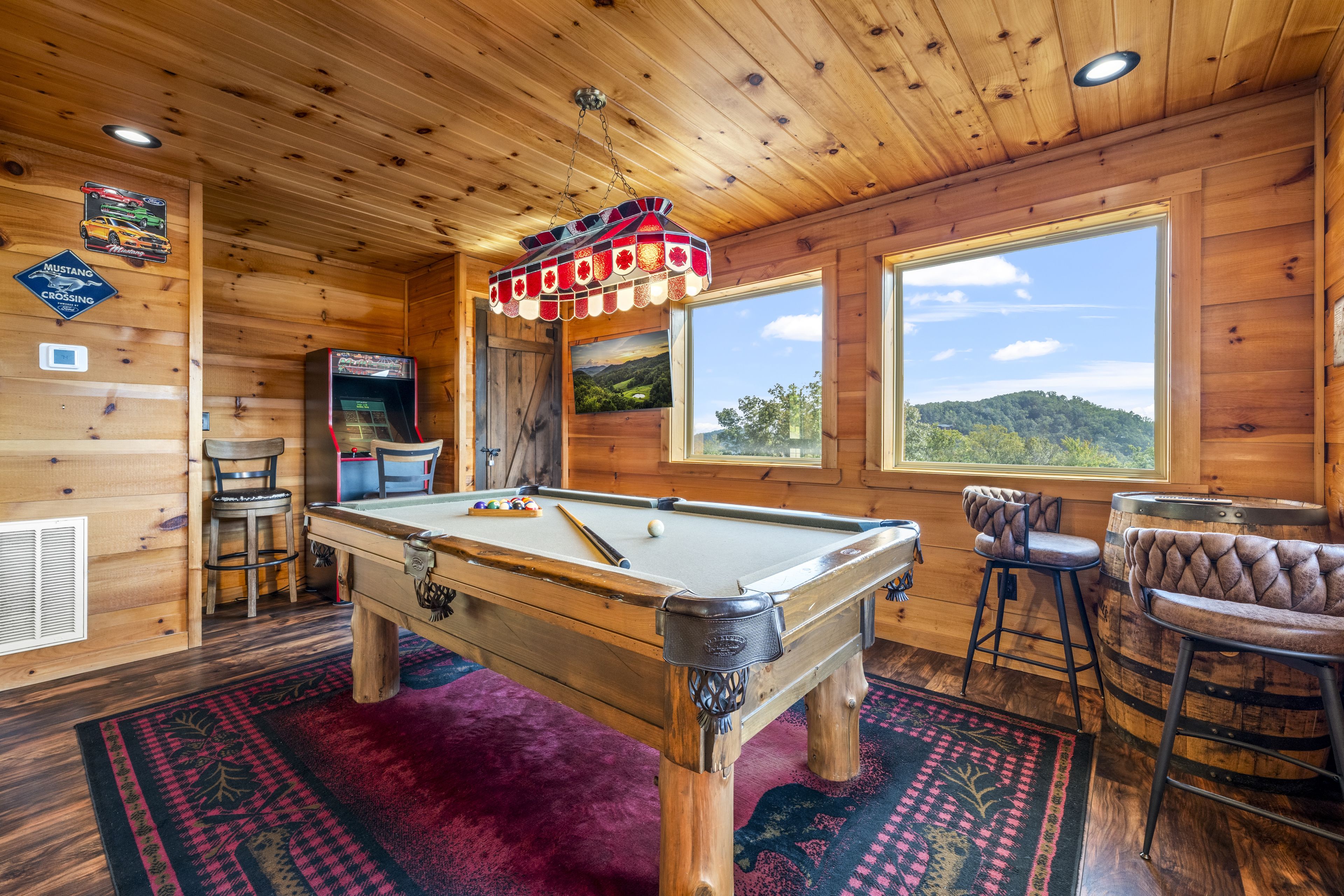 Un intérieur en bois avec une table de billard, des tabourets de bar et une vue sur l’extérieur.