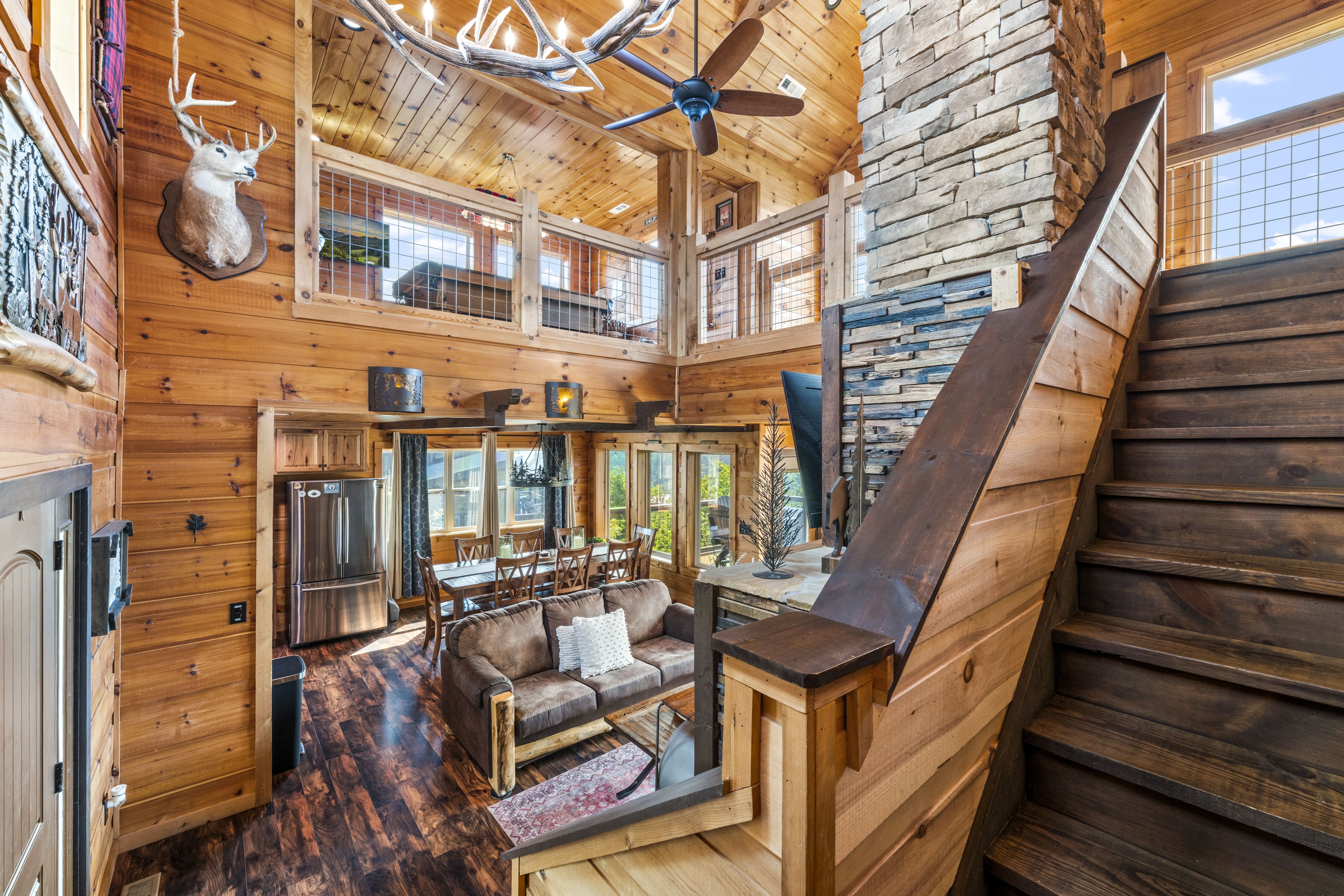 A spacious cabin interior with a dining area, a sofa, a ceiling fan, and a staircase.