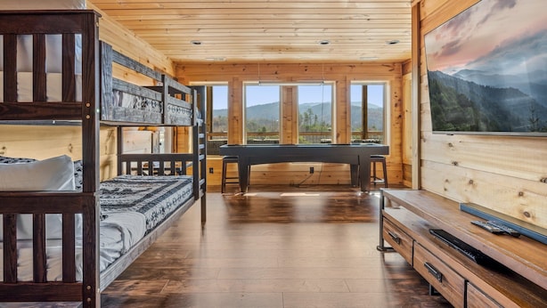 Ein Interieur einer Holzhütte mit Etagenbetten, einem Esstisch und einem Gemälde einer Berglandschaft.