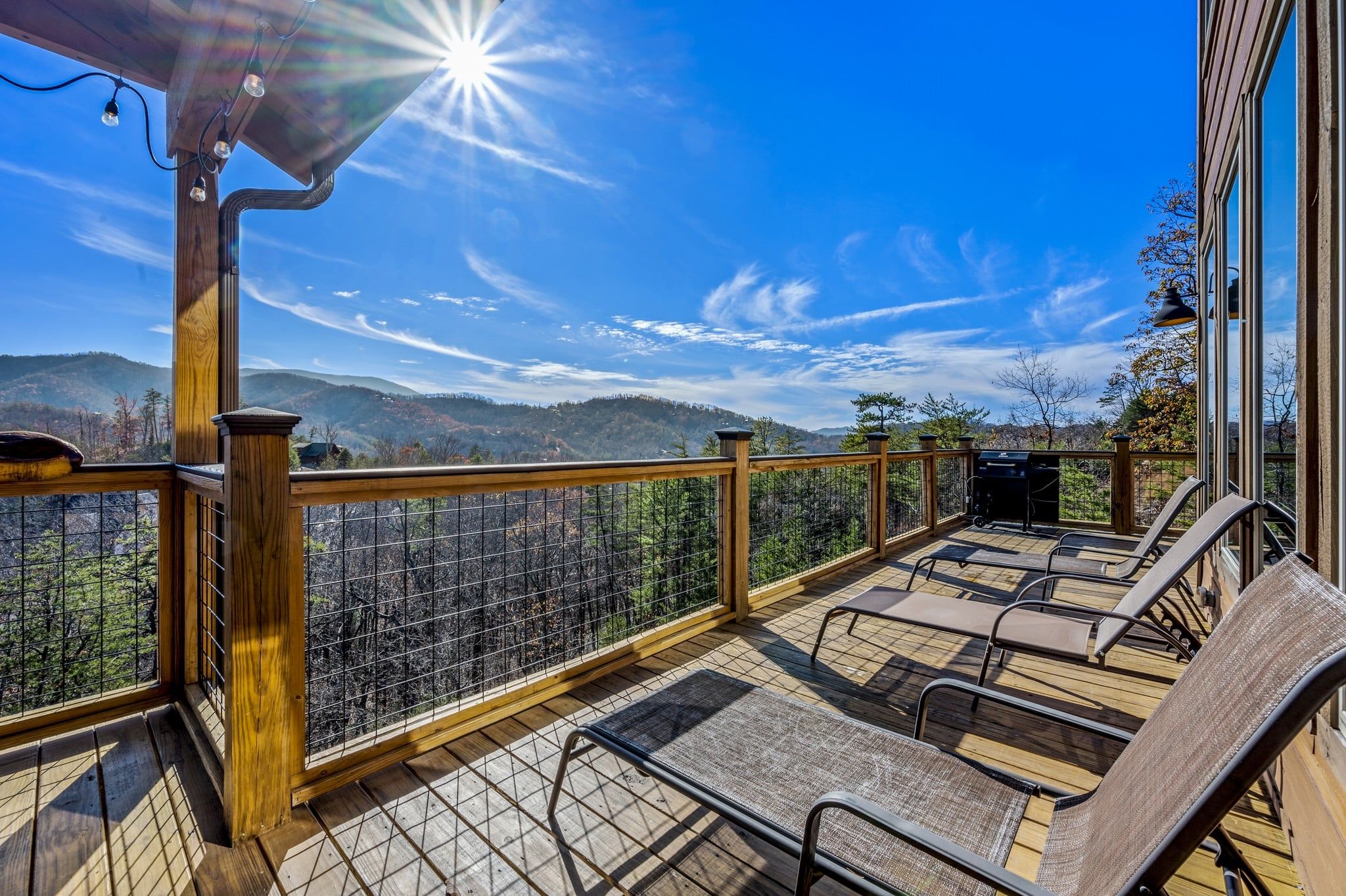 Terraza de madera con mobiliario exterior y vista a un paisaje montañoso.