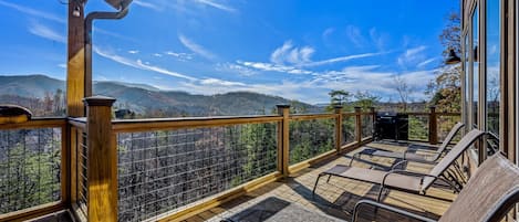 Terraza de madera con mobiliario exterior y vista a un paisaje montañoso.