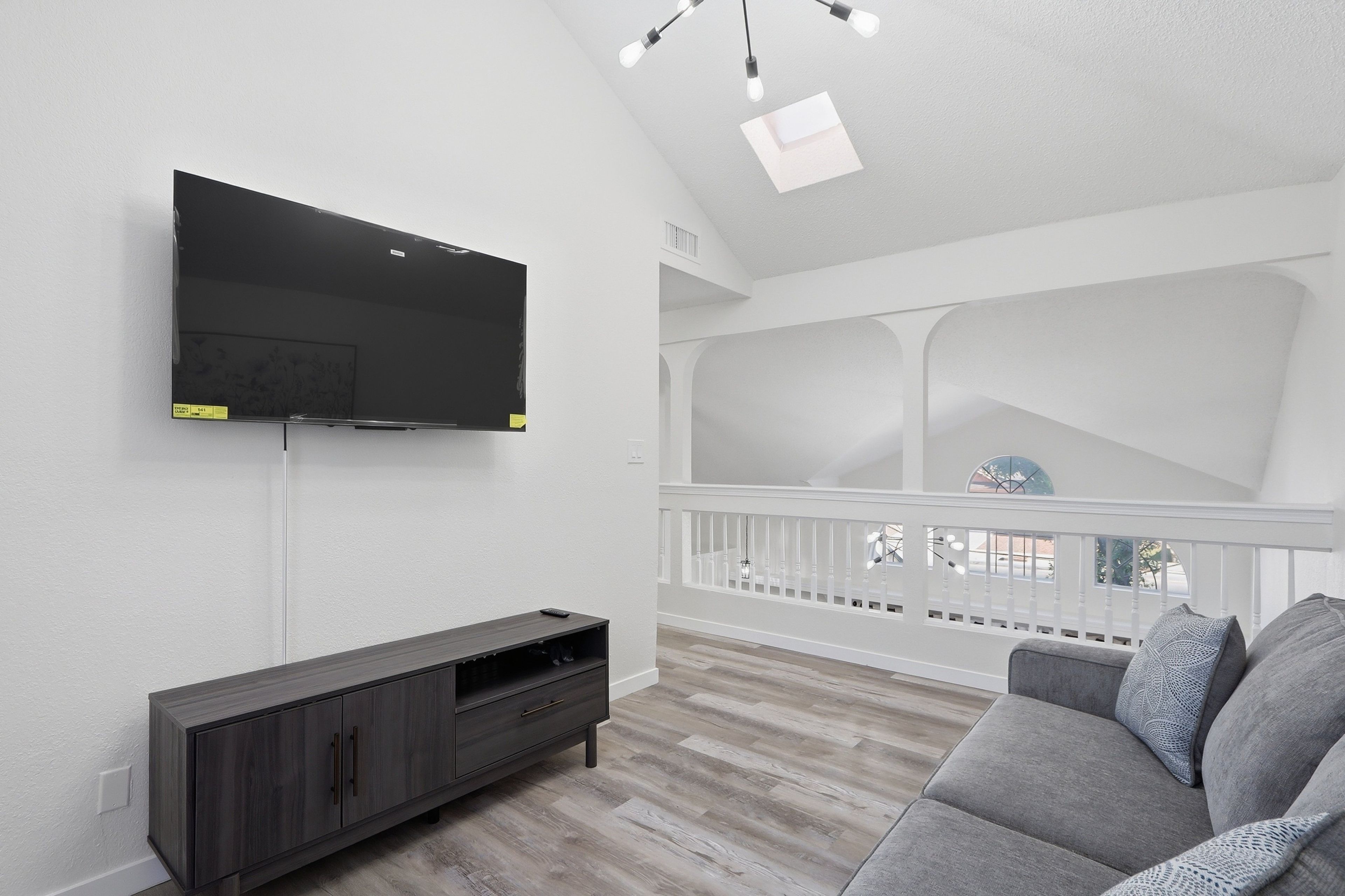 Una sala de estar con un televisor de pantalla plana montado en la pared, un mueble de entretenimiento de madera oscura y un sofá gris.