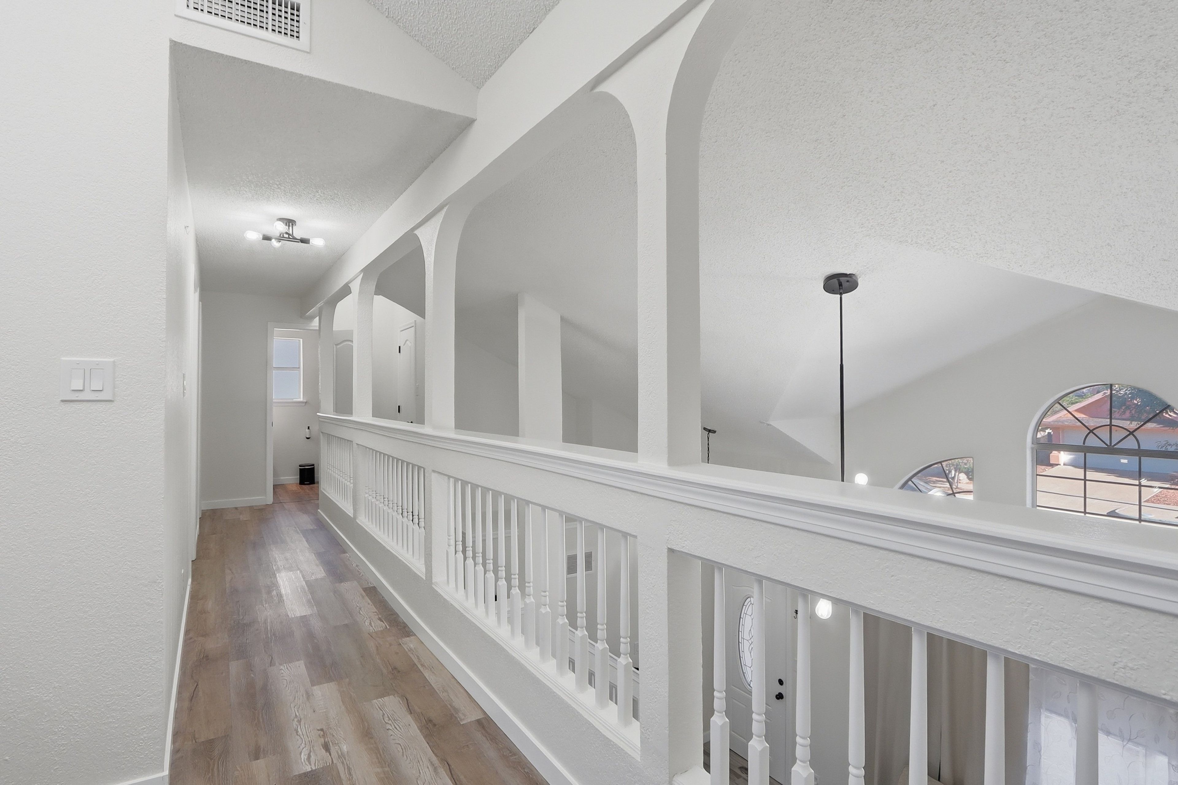 A spacious corridor with high ceilings and a wooden floor, leading to a room with a large window and a view of the outside.