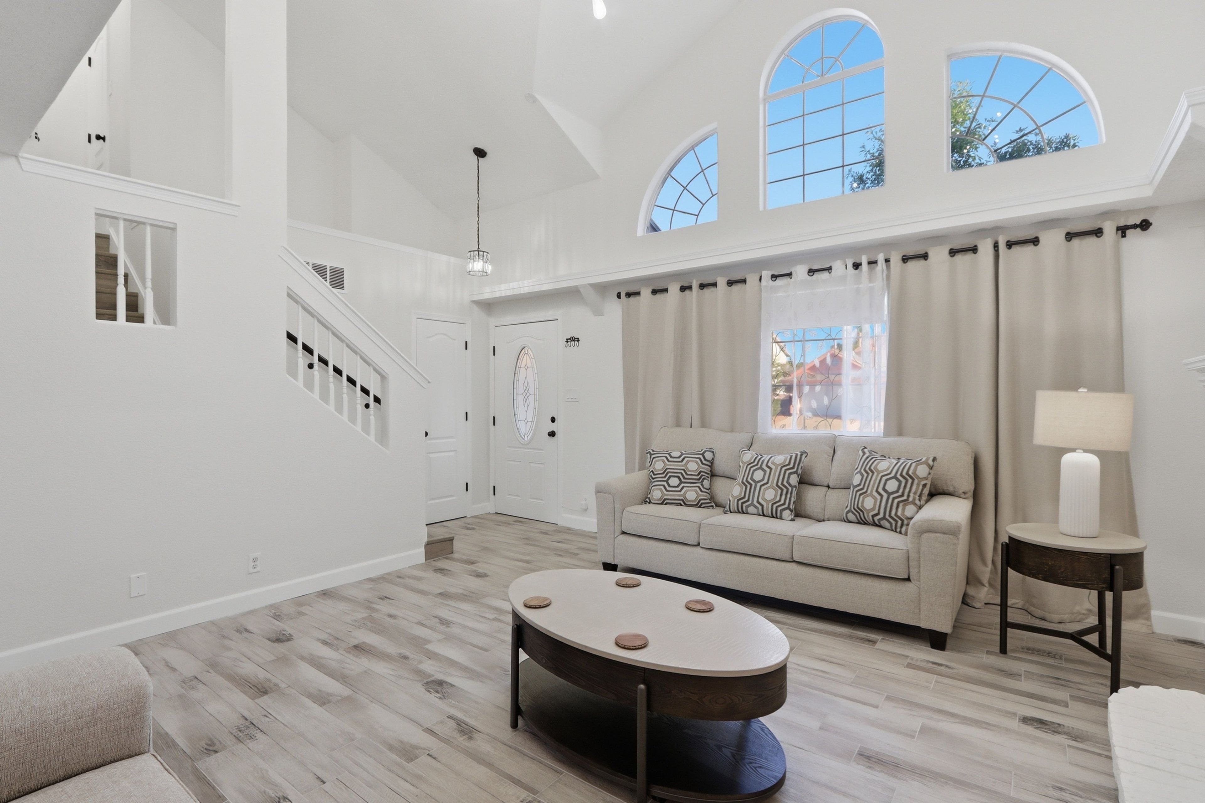 A spacious living area with a high ceiling, a staircase, and a large window.