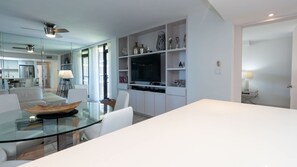 Una cocina moderna con una mesa de comedor de vidrio, armarios blancos y un televisor integrado.