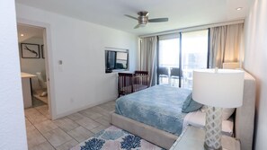 A hotel room with a bed, a desk, a chair, a TV, and a balcony with curtains. - Sea Vista Beachfront 3br - Heated Pool 3 Bedroom Apts (South Padre Island)