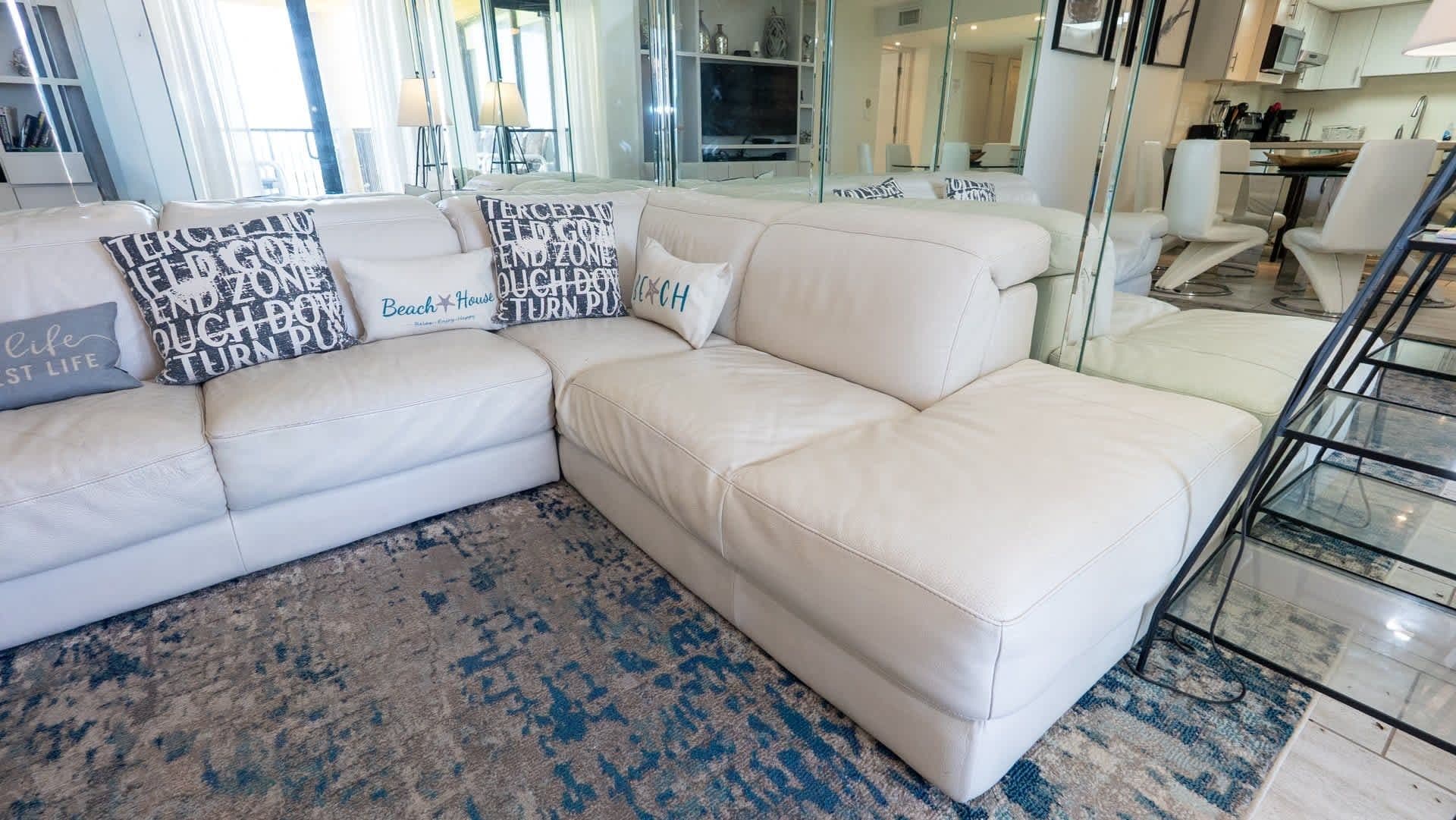 A white leather sectional sofa with multiple cushions, a patterned rug, and a glass railing in a modern living room.