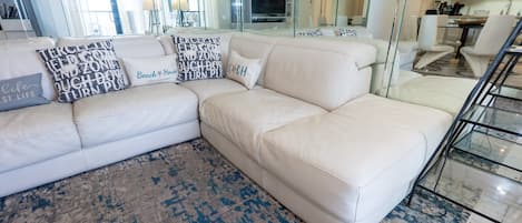Ein weißes, ledernes Ecksofa mit vielen Kissen, einem gemusterten Teppich und einem Glasgeländer in einem modernen Wohnzimmer.