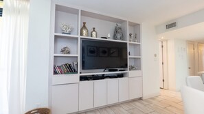A living room with a flat-screen TV, white shelving, and a white sofa. - Sea Vista Beachfront 3br - Heated Pool 3 Bedroom Apts (South Padre Island)