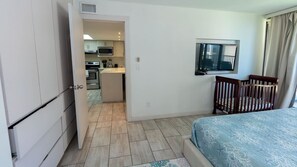 Habitación de hotel con cama, una silla de madera, un televisor y una kitchenette al fondo.