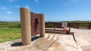 Una estructura de concreto con puerta de madera, un portón metálico y barandilla de madera con vistas a un paisaje cubierto de césped.