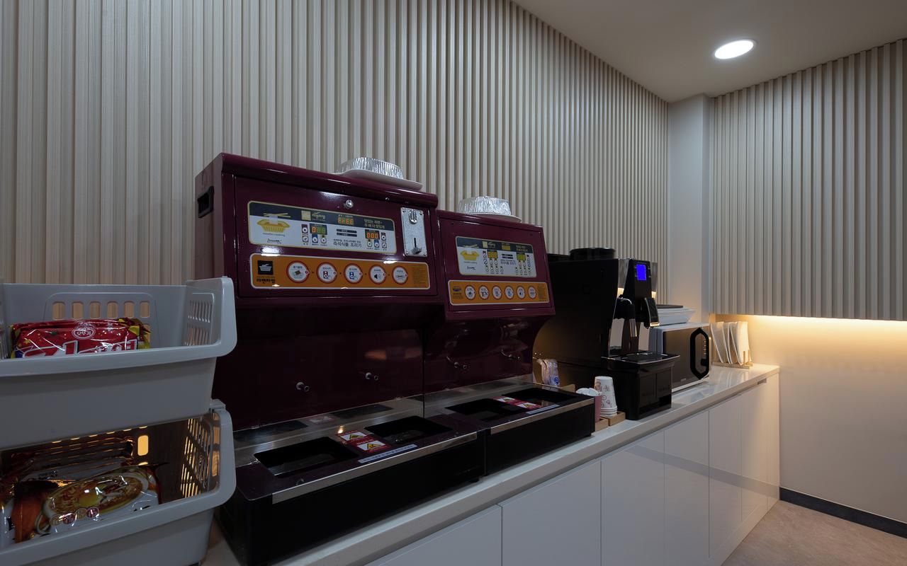 A coffee station with two espresso machines and a coffee maker, a snack bar with packaged snacks, and a microwave on a counter.