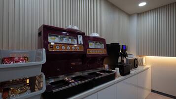 A coffee station with two espresso machines and a coffee maker, a snack bar with packaged snacks, and a microwave on a counter.