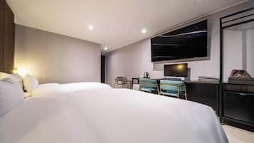 Ein modernes Hotelzimmer mit einem großen Bett, einem Schreibtisch mit zwei Stühlen, einem Flachbildfernseher und einer Minibar.