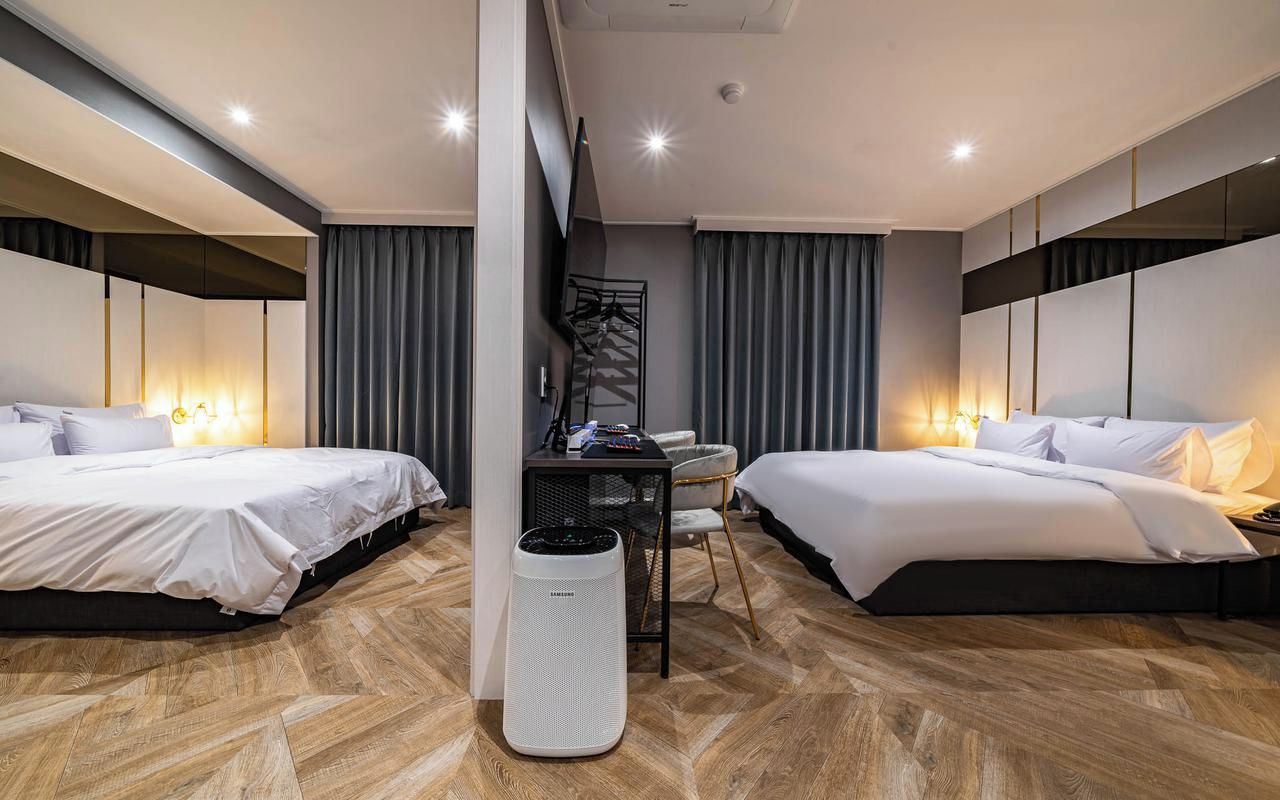 A hotel room with two beds, a desk, a chair, and a large air purifier.