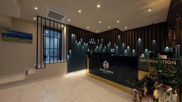 A hotel reception area with a modern design, featuring a reception desk, a wall-mounted information sign, and a large window.