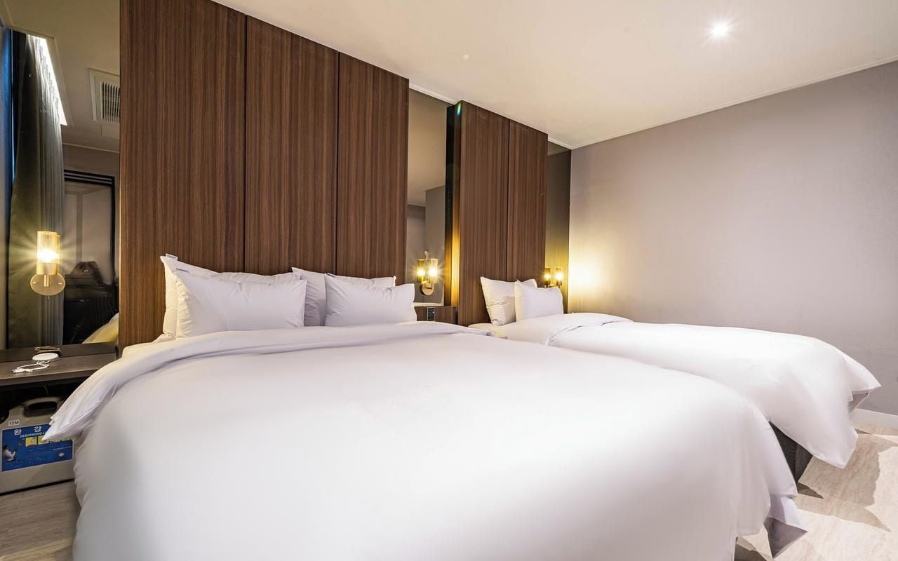 A hotel room with two beds, a large mirror, and wall-mounted lights.