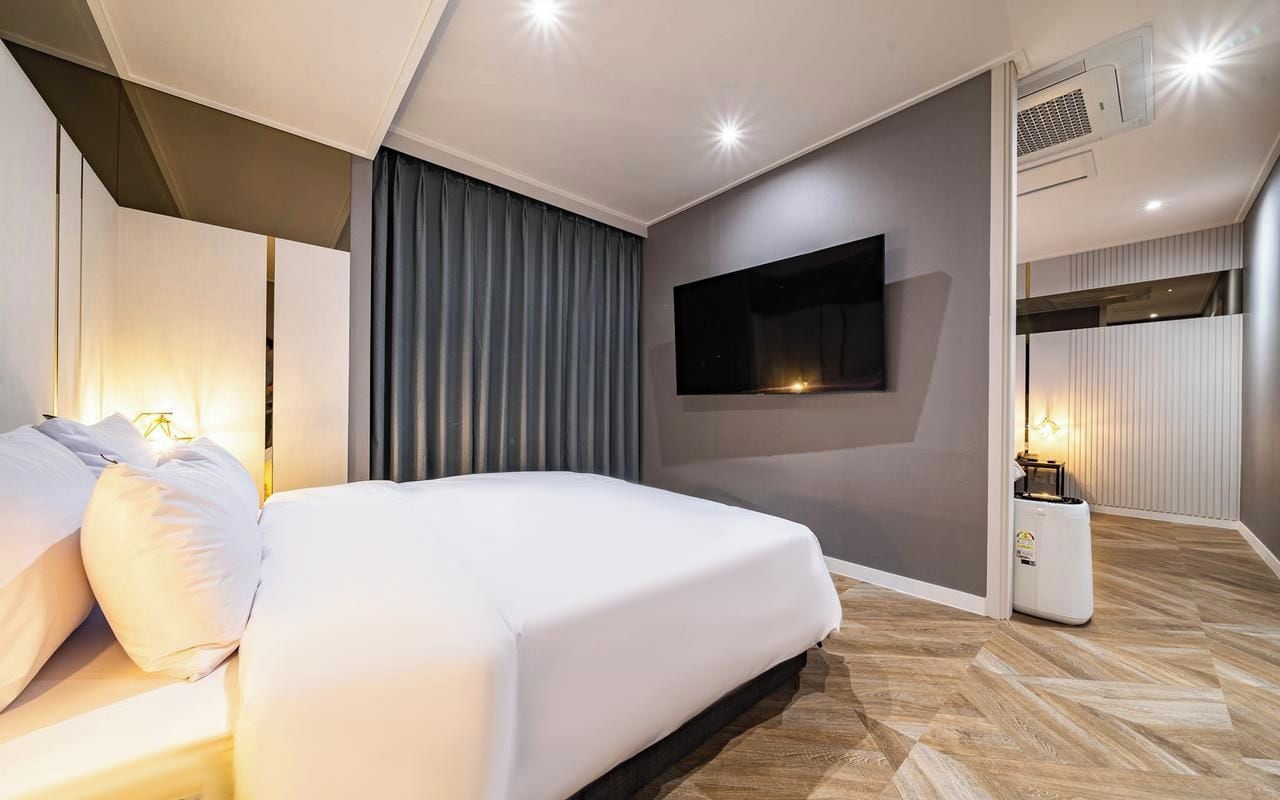 Une chambre d’hôtel moderne avec un grand lit, un téléviseur à écran plat fixé au mur et une table de chevet avec une lampe.