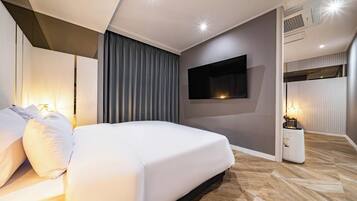 Une chambre d’hôtel moderne avec un grand lit, un téléviseur à écran plat fixé au mur et une table de chevet avec une lampe.