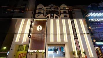 Entrada de hotel con un letrero destacado, un mostrador de recepción y un área de estacionamiento.