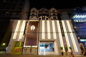 Entrada de hotel com placa chamativa, balcão de recepção e área de estacionamento.