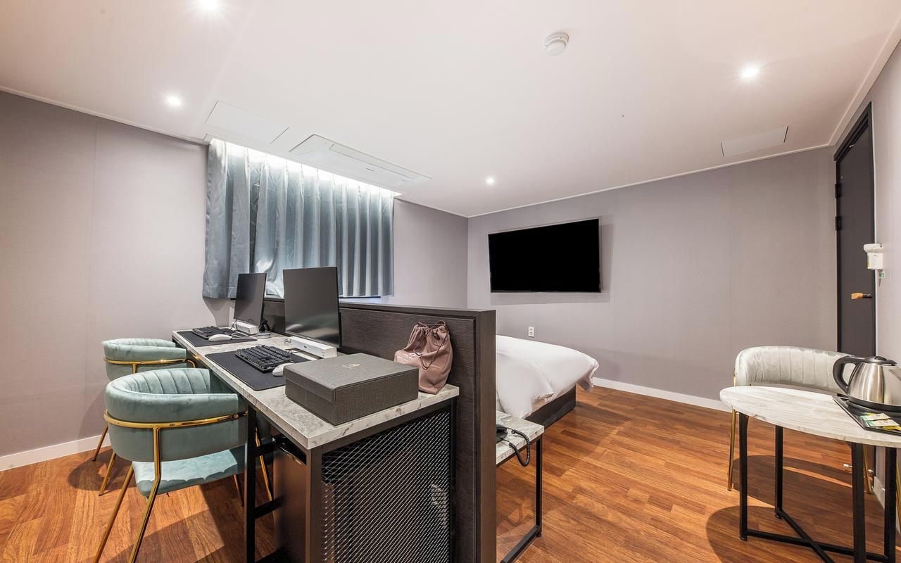 Una camera d'albergo moderna con una scrivania, due sedie, un letto, una TV e un piccolo tavolino con un bollitore.