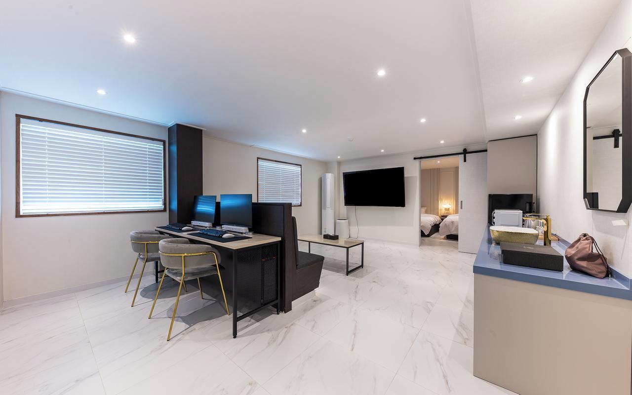 Una sala de estar moderna con un televisor de pantalla plana, un escritorio con una computadora y una zona de estar con dos sillones.